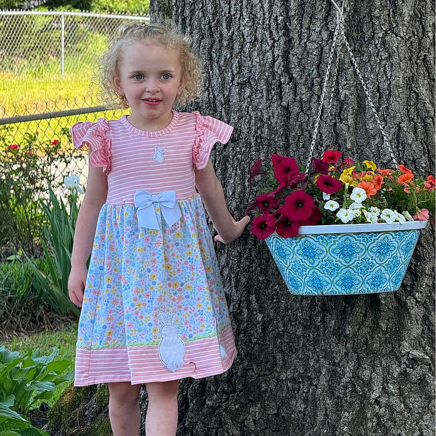Monica joined the competition — help win amazing prizes! bark, bow, bunny_applique, child, curly_hair, fence, floral_pattern, flower_pot, flowers, garden, girl, grass, greenery, nature, outdoor, pink_dress, plant, sandals, sunlight, tree
