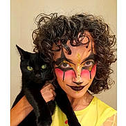 Lana participe au concours pour gagner de l'argent avec cette photo : person, cat, black_cat, curly_hair, face_paint, makeup, yellow_shirt, pet, animal, portrait, indoor, green_eyes, holding, looking_at_camera, close_up, expression, creative_makeup, costume, human, feline