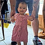 baby, child, pink_dress, barefoot, tattoo, adult, holding_hands, indoors, tiles, smile, floor, shorts, slippers, person, door, clothing, standing, support, happy, family