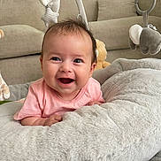 Amber is registered to the contest to win money with this photo: baby, smiling, face, infant, plush_toy, giraffe, elephant, cushion, pink_clothing, happy, indoor, person, child, soft_toy, head, cute, lying_down, furniture, home, bright