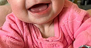 Della is registered to the contest to win money with this photo: baby, smiling, pink_clothing, teething_toy, cushion, indoor, happy, child, infant, face, portrait, cute, cozy, soft_texture, home, playful, young_child, expression, closeup, person