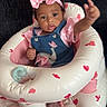 baby, infant, child, pink_bow, headband, denim_overall, elephant_embroidery, inflatable_seat, heart_pattern, candy_pattern, reaching_hand, cute, adorable, indoors, couch, soft_lighting, portrait, sitting, expression, young_child