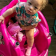 Journi is registered to the contest to win money with this photo: toddler, child, pink, toy_car, plush_toy, sitting, curly_hair, indoor, floor, sock, clothing, looking_up, cute, playtime, person, baby, seat, expression, colorful, wooden_floor