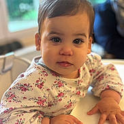 Judith participe au concours pour gagner de l'argent avec cette photo : toddler, child, face, expression, highchair, clothing, floral_pattern, hand, indoor, portrait, person, skin, hair, eyes, table, furniture, baby, cute, young, cozy