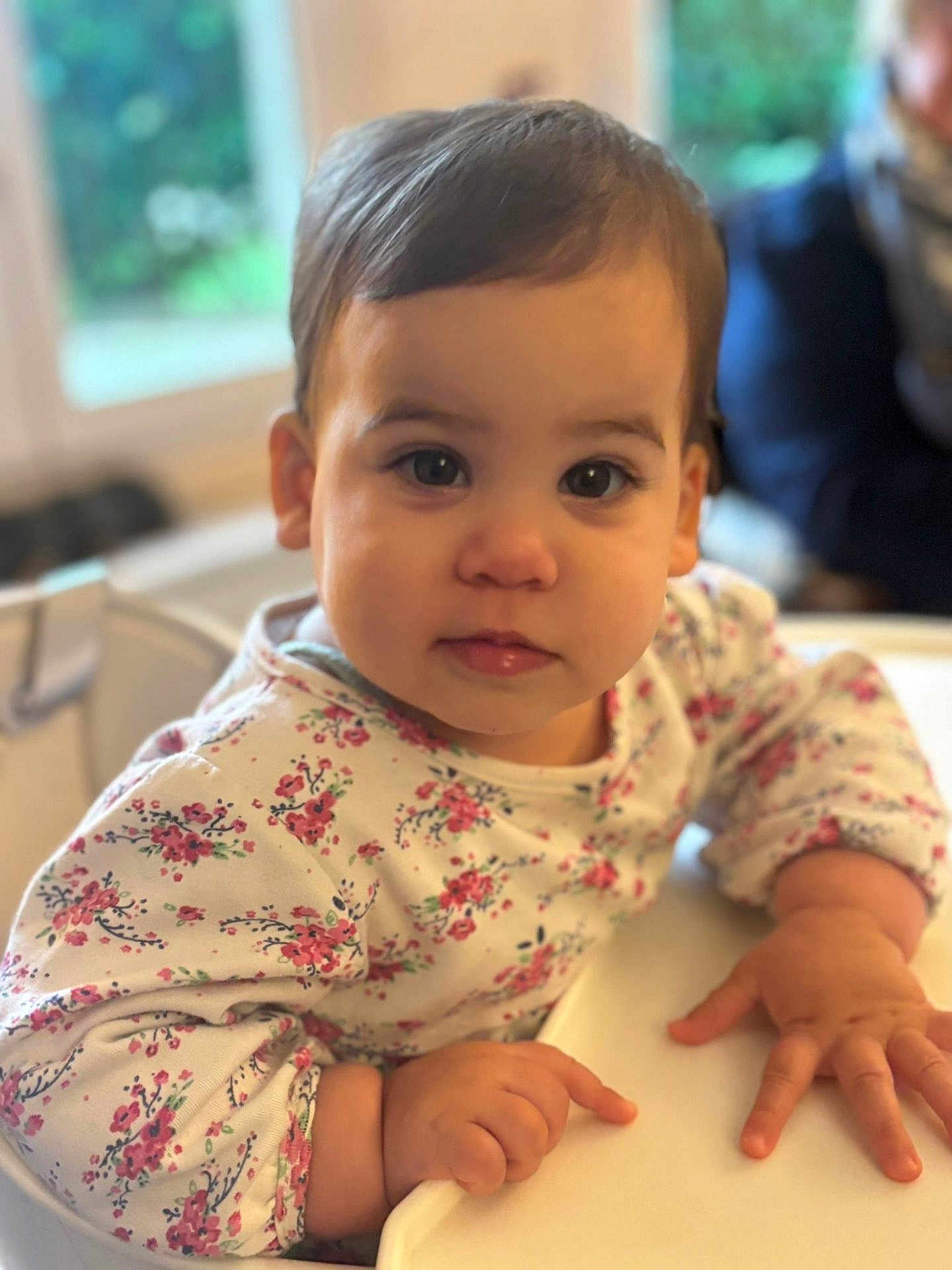 Judith participe au concours pour gagner de l'argent avec cette photo : toddler, child, face, expression, highchair, clothing, floral_pattern, hand, indoor, portrait, person, skin, hair, eyes, table, furniture, baby, cute, young, cozy