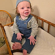 Greyson is registered to the contest to win money with this photo: baby, barefoot, blue_cap, child, crib, cushion, cute, denim_overalls, face, happy, home, indoor, person, plaid_shirt, portrait, sitting, smiling, toddler, wooden_furniture, young_child