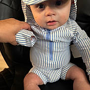 Waylon is registered to the contest to win money with this photo: baby, child, striped_clothing, hat, blue_and_white, sitting, hand, black_chair, curious_expression, young_child, portrait, infant, cute, indoors, closeup, person, clothing, face, headwear, seated