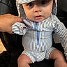 baby, child, striped_clothing, hat, blue_and_white, sitting, hand, black_chair, curious_expression, young_child, portrait, infant, cute, indoors, closeup, person, clothing, face, headwear, seated