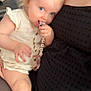 toddler, child, blue_eyes, hair_clip, pacifier_clip, snuggling, adult, black_dress, indoor, cute, baby, hand, face, skin, person, close_up, comfort, holding, seated, light