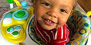 Tyrone is registered to the contest to win money with this photo: baby_walker, bright, carpet, child, colorful, curly_hair, cute, face, footwear, furniture, happy, home, indoor, person, playful, red_striped_clothing, smiling, sock, toddler, toy