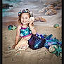 child, girl, mermaid_costume, seashell, starfish, beach, sand, smile, portrait, costume, jewelry, bracelet, necklace, headband, underwater_theme, ocean_backdrop, playful, happy, pose, photography