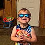child, boy, sunglasses, smile, indoor, paw_patrol, tank_top, wood_paneling, door, carpet, chair, toy, happy, portrait, casual, furniture, reflection, colorful, cute, hands
