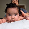 baby, infant, face, person, skin, hair, chubby_cheeks, expression, eyes, blurred_background, adult, supporting_hand, cushion, white, indoor, portrait, closeup, soft_light, curly_hair, cute