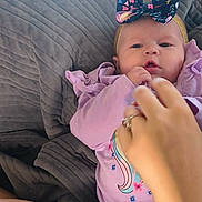 Rylie Miller is registered to the contest to win money with this photo: adult_hand, baby, blanket, blue, bow, clothing, cozy, cute, floral_pattern, hand, headband, indoor, infant, lying_down, pacifier, person, pink, purple, toddler, unicorn