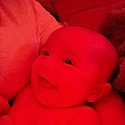 Grace is registered to the contest to win money with this photo: baby, infant, smiling, smile, portrait, close_up, red_tint, soft_lighting, bare_torso, head, eyes, cheeks, arm, couch, blanket, indoor, parent, holding, happy, young_child