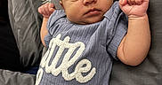 Jhire is registered to the contest to win money with this photo: baby, bed, blanket, clothing, cute, face, fist, indoor, infant, lying_down, newborn, onesie, person, pillow, portrait, rest, skin, sleepwear, soft, text_on_clothing