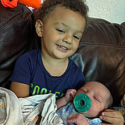 Jaden joined the competition — help win amazing prizes! toddler, baby, pacifier, blanket, couch, child, smiling, curly_hair, indoor, family, holding, comfort, sleepy, blue_clothing, leather, orange_bag, portrait, sibling, cute, happy