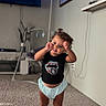 Jaycie joined the competition — help win amazing prizes! toddler, child, barefoot, carpet, living_room, black_tshirt, graphic_tee, blue_shorts, smiling, standing, indoor, lamp, television, wall_art, furniture, home, cute, playful, person, happy