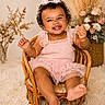 baby, basket, bow, carpet, child, cozy, curly_hair, cute, decor, floral_arrangement, fun, happy, indoor, pink_dress, portrait, sitting, smiling, toddler, wicker_chair, young_child