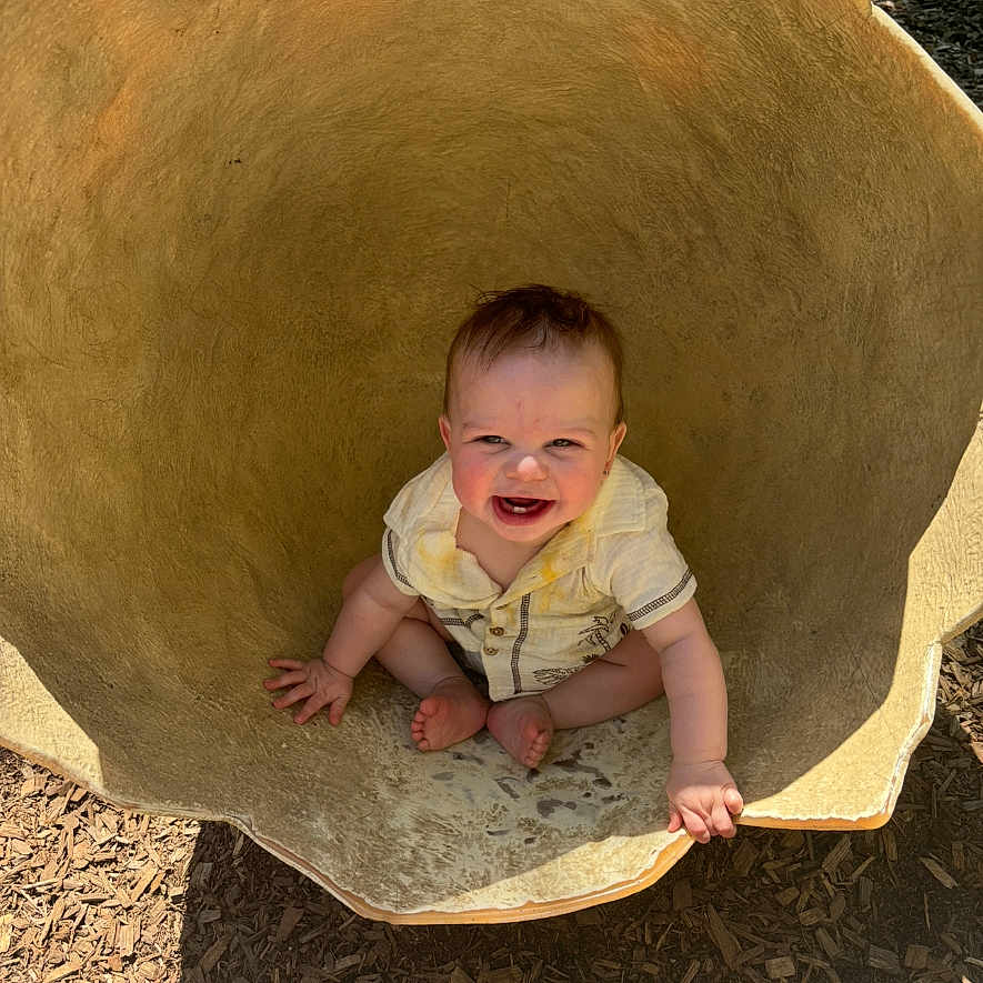 Ronyn joined the competition — help win amazing prizes! baby, child, clothing, cute, daylight, expression, face, hand, happy, head, large_bowl, nature, outdoor, playground, sitting, skin, smiling, sunlight, toes, wood_chips