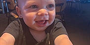Ronyn is registered to the contest to win money with this photo: baby, child, smile, happy, face, hair, earring, black_shirt, table, restaurant, chair, background, television, indoor, person, cute, expression, young_child, skin, light