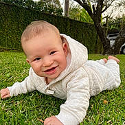 Keon is registered to the contest to win money with this photo: baby, child, grass, outdoor, hoodie, white_clothing, smile, crawling, greenery, tree, nature, daylight, face, person, infant, quilted_fabric, park, cute, young_child, garden