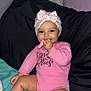 baby, child, pink_onesie, headwrap, teething_toy, smiling, sitting, indoor, pillow, bed, blanket, cute, infant, happy, skin, hand, foot, sock, face, person