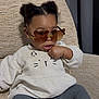 toddler, child, sunglasses, heart_shaped_glasses, sweater, cat_design, seated, chair, indoors, curly_hair, fashion, cute, cozy, portrait, young_child, casual_clothing, expression, comfortable, home, relaxed