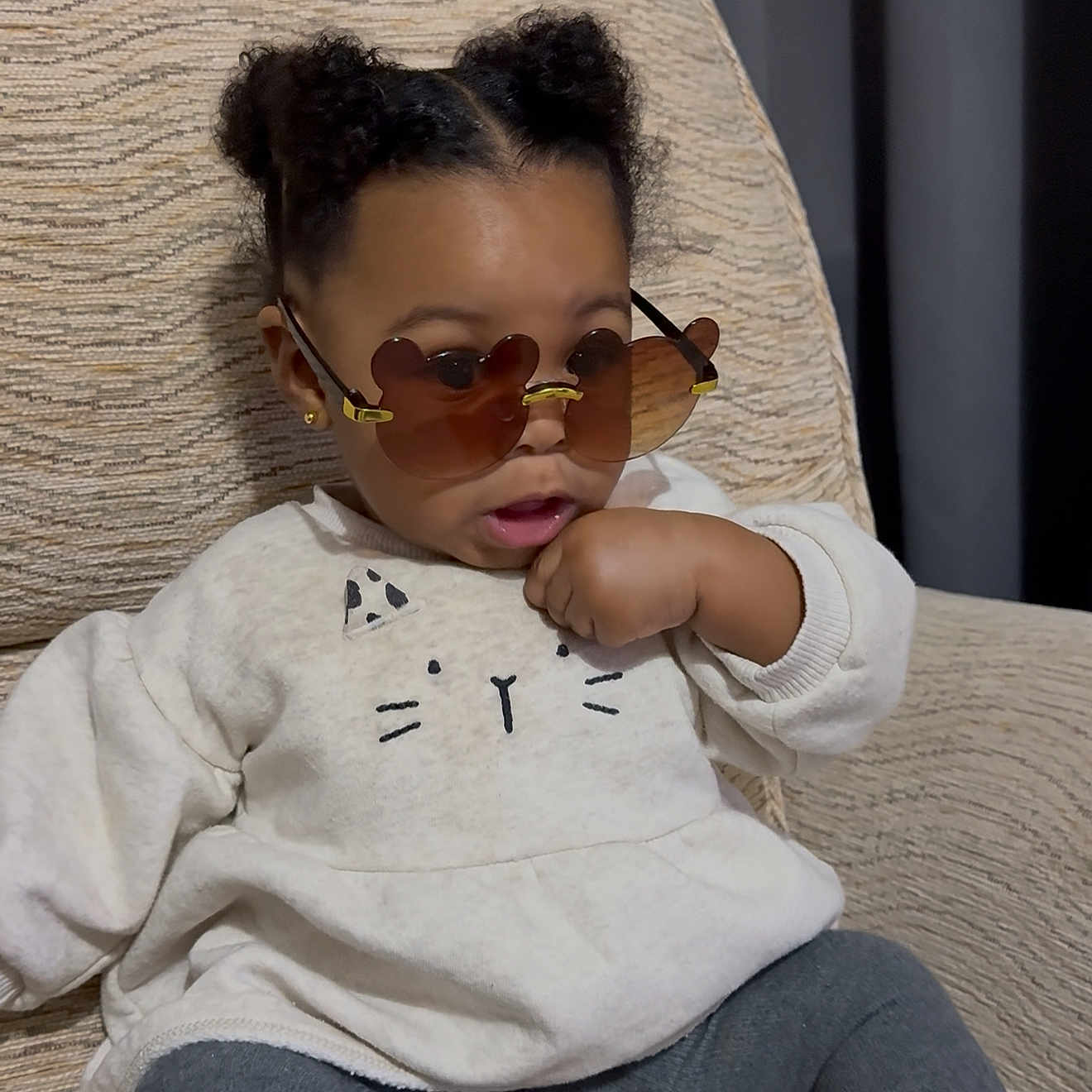 Primrose is registered to the contest to win money with this photo: casual_clothing, cat_design, chair, child, comfortable, cozy, curly_hair, cute, expression, fashion, heart_shaped_glasses, home, indoors, portrait, relaxed, seated, sunglasses, sweater, toddler, young_child