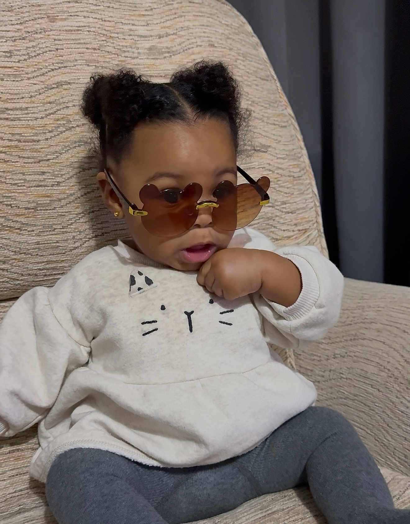 Primrose is registered to the contest to win money with this photo: toddler, child, sunglasses, heart_shaped_glasses, sweater, cat_design, seated, chair, indoors, curly_hair, fashion, cute, cozy, portrait, young_child, casual_clothing, expression, comfortable, home, relaxed