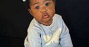 Janayah is registered to the contest to win money with this photo: baby, blue_clothing, bow, child, cozy, curious, cute, dark_background, expression, face, indoors, infant, knitted_outfit, person, portrait, sitting, small_hands, soft_lighting, white_bow, young
