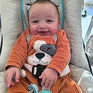 Naïm a rejoint le concours — aidez-le/la à gagner de superbes lots ! animal_print, baby, baby_seat, cat, child, cushion, cute, face, floor_tile, hand, happy, indoor, infant, onesie, orange_clothing, pacifier, person, smile, sunlight, window