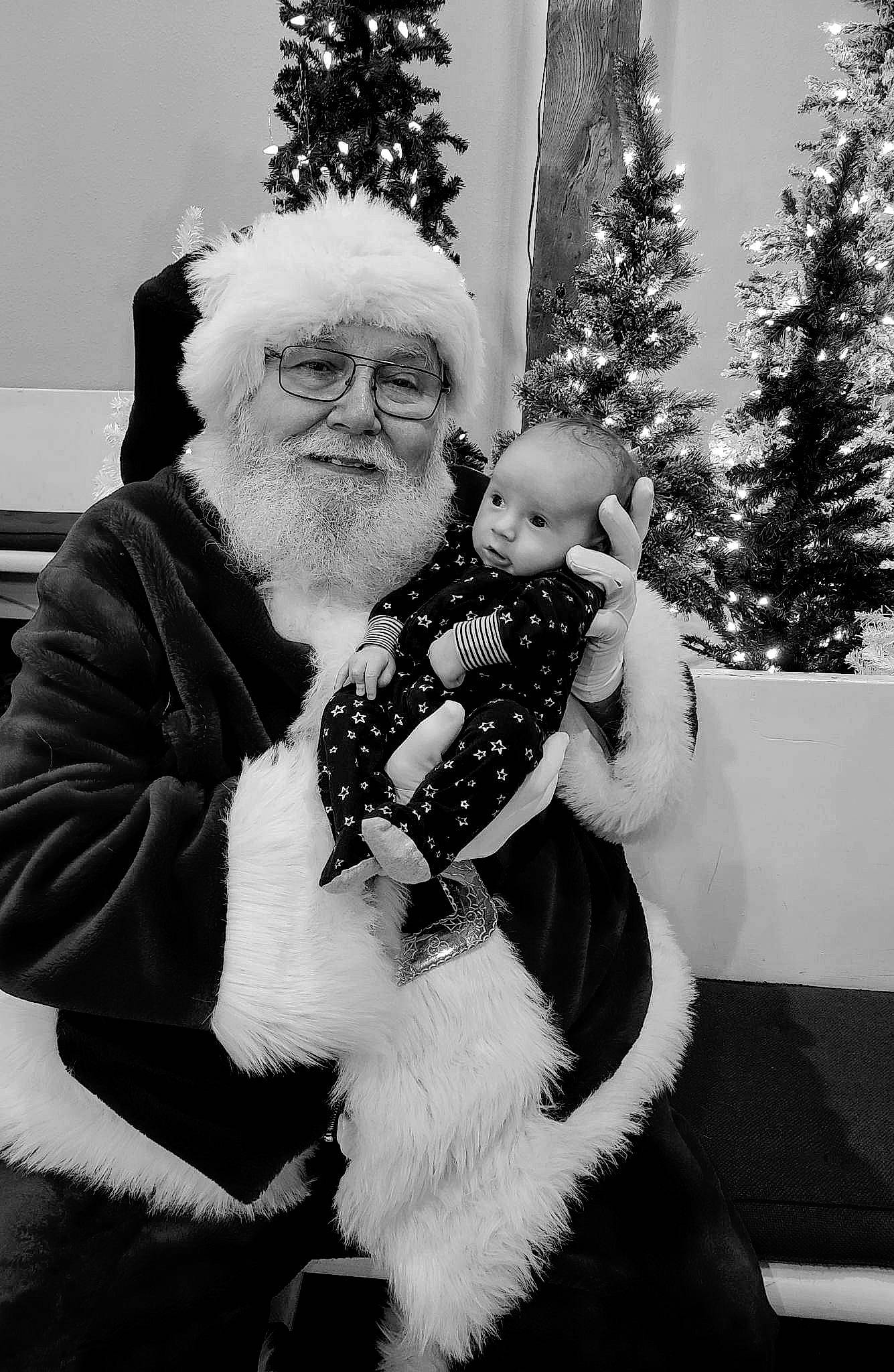 Kelly is registered to the contest to win money with this photo: beard, black, black_and_white, christmas_tree, event, fun, fur_clothing, happy, hat, headwear, holiday, human_body, lap, monochrome, monochrome_photography, person, santa_claus, standing, style, tree