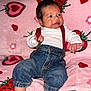 baby, infant, denim_pants, red_suspender, white_shirt, pink_blanket, strawberry_pattern, heart_pattern, cute, smiling, sitting, indoors, soft_texture, child, face, person, clothing, footwearless, cozy, portrait