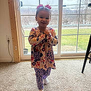 Myah joined the competition — help win amazing prizes! child, toddler, smiling, dress, hair_bows, window, sliding_door, carpet, indoor, outdoor_view, grass, trees, standing, socks, patterned_clothing, happy, portrait, natural_light, floor, home_interior