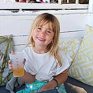 Romy a rejoint le concours — aidez-le/la à gagner de superbes lots ! child, girl, smile, blonde_hair, white_shirt, plastic_cup, drink, cushion, bench, outdoor, canopy, table, happy, casual, daylight, relaxing, seating, people_in_background, bracelet, park