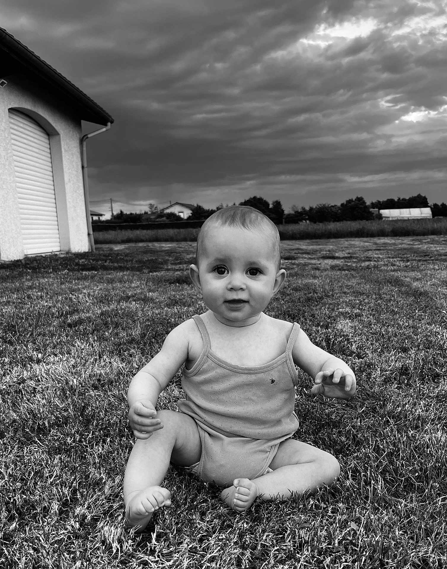 Louise a rejoint le concours — aidez-le/la à gagner de superbes lots ! baby, child, grass, outdoor, cloudy_sky, field, house, onesie, sitting, portrait, curious, nature, daylight, person, barefoot, expression, landscape, young, summer, monochrome
