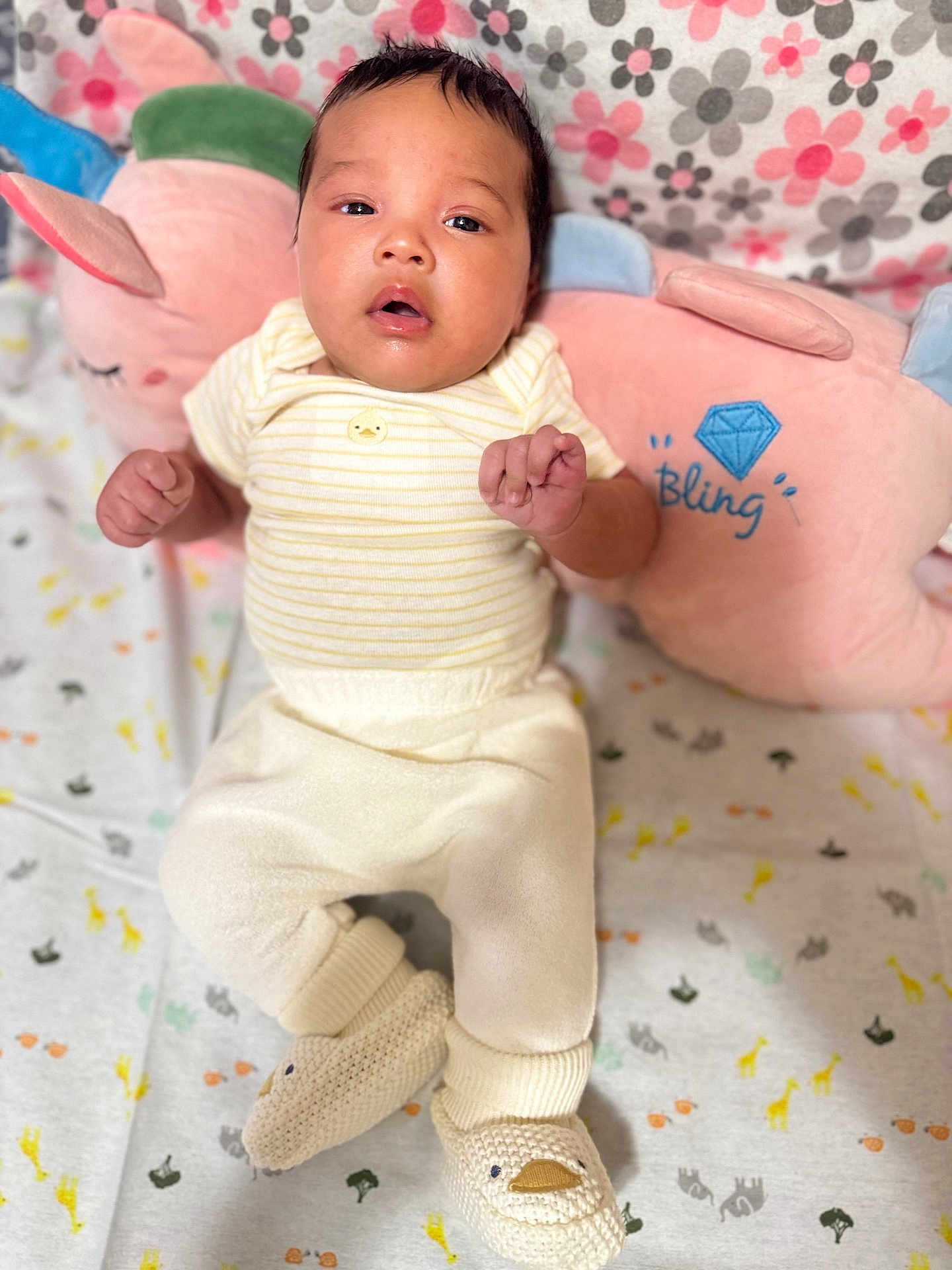 Jasmine is registered to the contest to win money with this photo: baby, infant, plush_pillow, blanket, pattern, animal_print, duck_booties, clothing, cute, lying_down, soft_toys, pink_pillow, yellow_stripes, face, hand, footwear, bedroom, child, cozy, indoor