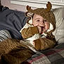 baby, child, onesie, hood, antlers, bed, blanket, plaid, hand, smile, indoor, cozy, cute, infant, face, clothing, young, person, lying_down, warm