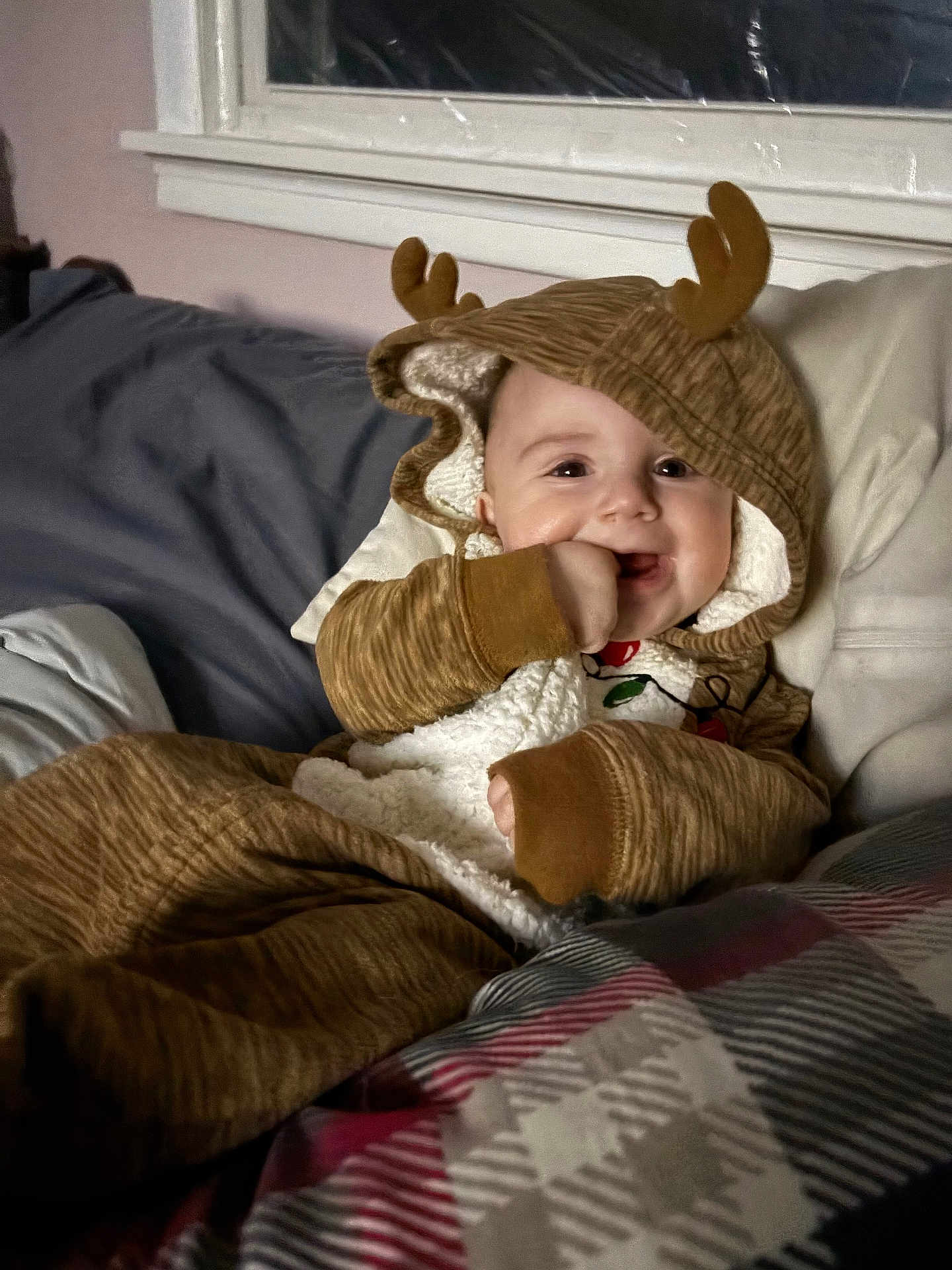 Lila joined the competition — help win amazing prizes! baby, child, onesie, hood, antlers, bed, blanket, plaid, hand, smile, indoor, cozy, cute, infant, face, clothing, young, person, lying_down, warm