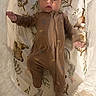 Logan is registered to the contest to win money with this photo: baby, infant, child, portrait, lying_down, bassinet, crib, nursery, brown_outfit, jumpsuit, zipper, pacifier, bedding, blanket, woodland_pattern, soft_lighting, indoor, reaching, wide_eyed, baby_face