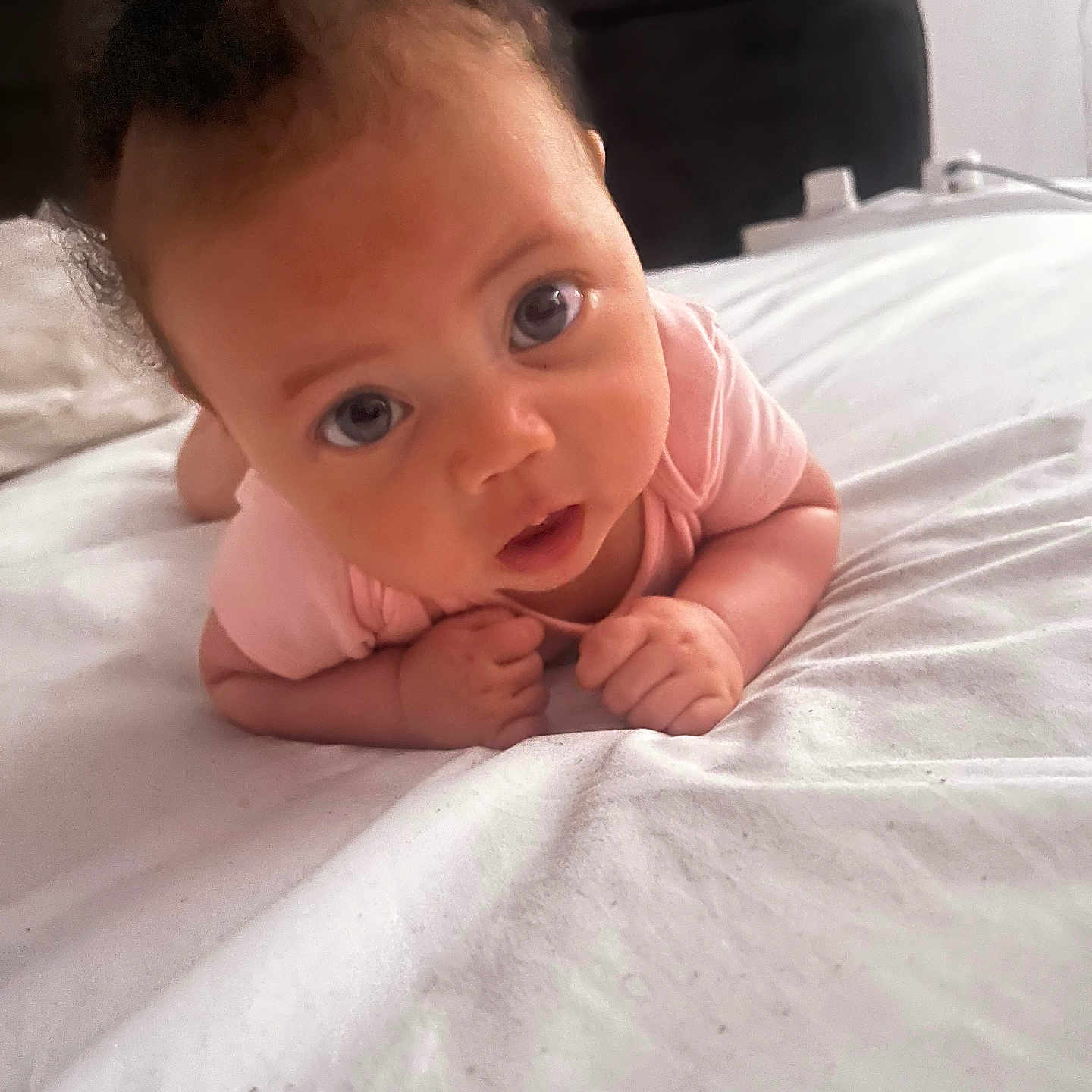 Azriah is registered to the contest to win money with this photo: baby, bed, candid, child, curious, expression, eyes, face, hands, head, indoor, infant, person, pink_onesie, portrait, resting, skin, tummy_time, white_bedspread, young