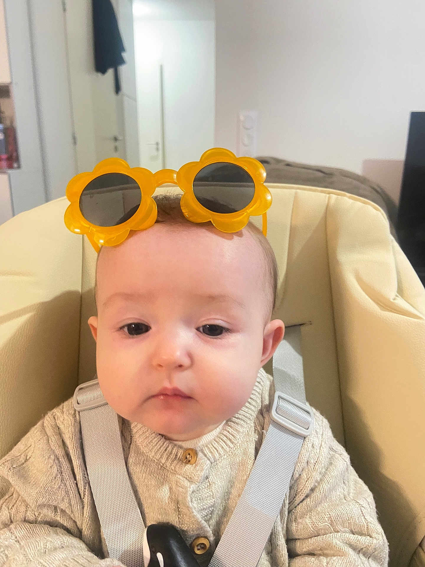 Emma participe au concours pour gagner de l'argent avec cette photo : baby, child, sunglasses, yellow, flower_shaped, knitted_sweater, beige_seat, harness, indoor, neutral_expression, face, person, young_child, cute, clothing, headwear, seat, baby_seat, closeup, young_baby