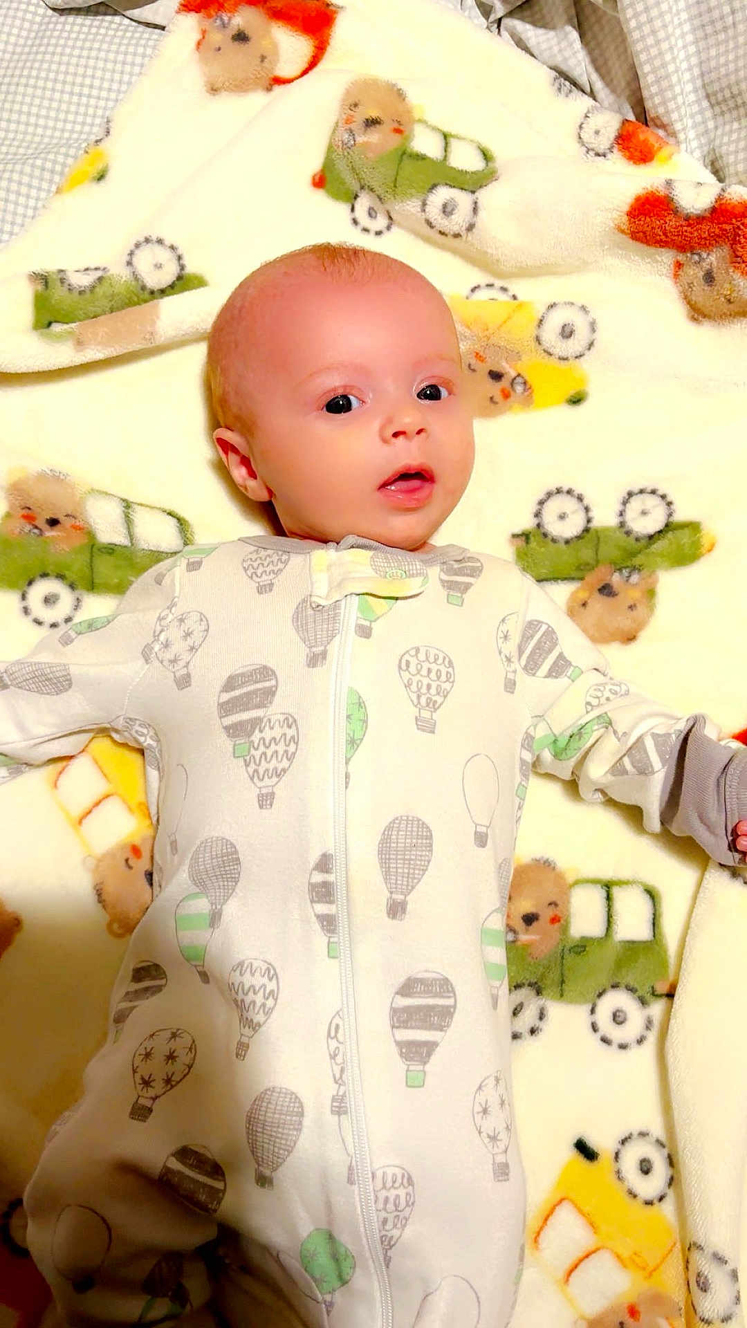 Abel joined the competition — help win amazing prizes! baby, infant, onesie, blanket, pattern, hot_air_balloon, car, bear, cute, lying_down, indoors, child, soft, cozy, sleepwear, young, portrait, curious, face, person