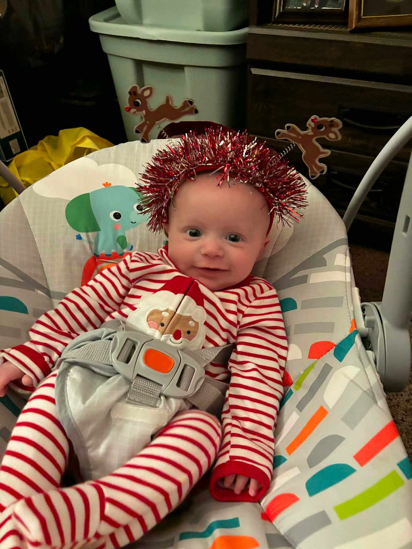 Abel is registered to the contest to win money with this photo: baby, baby_rocker, carpet, child, colorful_pattern, cute, festive, furniture, happy, headband, holiday, indoor, infant, portrait, red_striped_pajamas, reindeer, santa_claus, seatbelt, smiling, tinsel