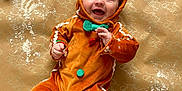 Oscar is registered to the contest to win money with this photo: baby, child, gingerbread_costume, smiling, happy, holiday, christmas, wrapping_paper, rolling_pin, flour, cookie_dough, gingerbread_man, cute, infant, festive, playful, orange_outfit, green_bow, red_buttons, background