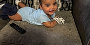 Benjamin joined the competition — help win amazing prizes! baby, child, smiling, couch, sofa, remote_control, mittens, socks, onesie, patterned_fabric, cushion, indoor, happy, infant, person, furniture, cozy, lying_down, head, cute