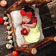Ariel is registered to the contest to win money with this photo: baby, sleeping, snow_white_costume, red_bow, yellow_dress, wooden_bed, knit_blanket, apple, toy_figures, seven_dwarfs, floor, wooden_floor, footwear, infant, cute, portrait, fairy_tale, costume, indoor, decor