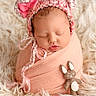 newborn, baby, sleeping, knitted_hat, bear_ears, pink_bow, blanket, soft_texture, fluffy_rug, felt_toy, bunny, cute, wrapped, portrait, infant, peaceful, cozy, child, indoors, adorable