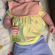 Bayley is registered to the contest to win money with this photo: baby, child, smiling, yellow_shirt, purple_pants, bib, blanket, patterned_blanket, lying_down, happy, infant, cute, soft_lighting, indoors, person, small_hands, pink_socks, face, cheerful, toddler